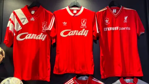 Three red Liverpool shirt hung against a black background