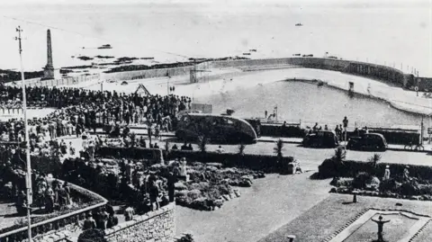 Jubilee Pool Black and white image of the Jubilee Pool in Cornwall. The image shows hundreds of people standing at the edge of the pool. Cars are parked around the edge.