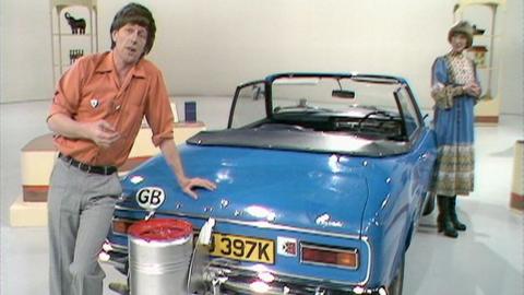 John Noakes leaning on the boot of the blue petrol-powered car, with Lesley Judd in the background.