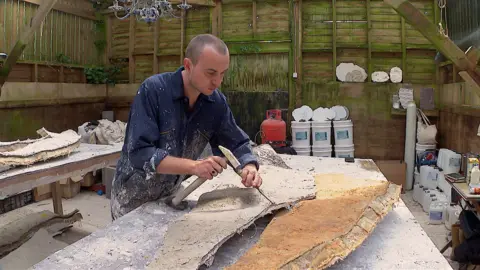 Artist, Robin Sullivan, using a hammer and chisel to take off the edges of one of the bronze panels which will cover the monoliths