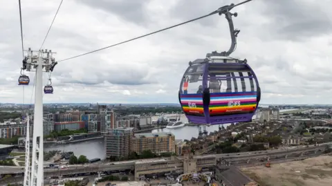 A rainbow-coloured cable car cabin sponsored by IFS hanging over London with the River Thames visible beneath.