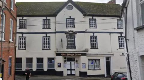 A large three story white building with a dark sign saying The Kings Arms above a black and white door