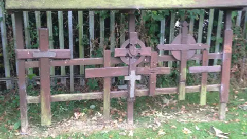 Cheltenham Civic Society A collection of six wooden crosses of different shapes and sizes, attached to a wooden frame in the cemetery