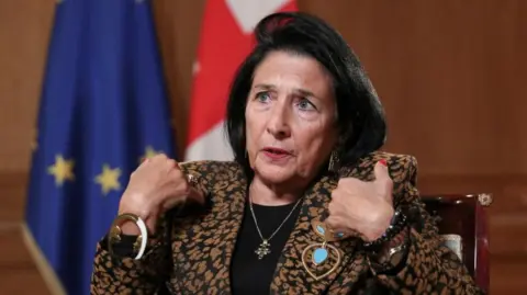 Reuters Georgia's President Salome Zourabichvili gestures during an interview as she sits in front of her country's flag and the EU flag