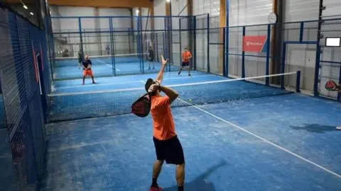 Getty Images People playing padel on a blue indoor court.