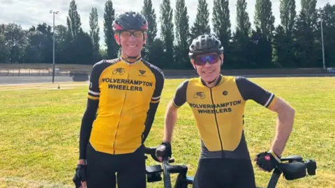 Jodie Parker Two men wearing mainly yellow tops including the words Wolverhampton Wheelers. They are wearing glasses and cycling helmets and a large area of grass and trees are in the background.