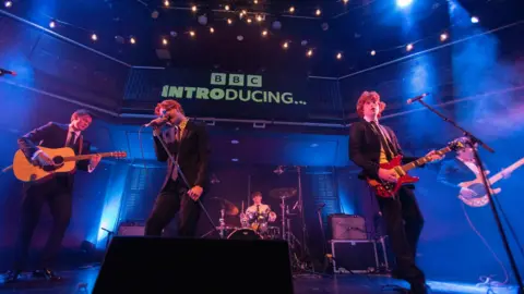 Swindled play the Glasshouse in Gateshead. The band members are dressed in suits and are holding musical instruments. Above the stage is the logo for BBC Introducing...
