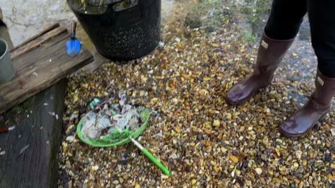 Some scattered items in the waterlogged garden. There is a net full of debris. Susannah is seen wearing wellies.
