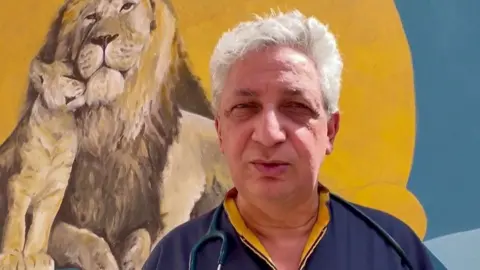 Head and shoulders shot of Dr Domenico Cipolla standing in front of a mural as he speaks to camera