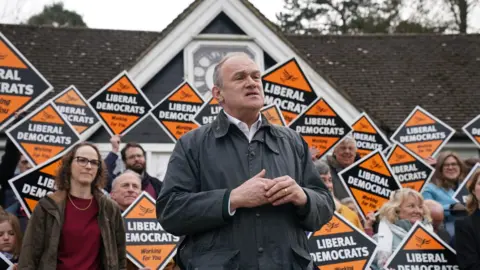 PA Media Liberal Democrat leader Sir Ed Davey is at a rally for Liberal Democrat activists in Haywards Heath. Campaigners stand behind him in a group, carrying Liberal Democrat placards.