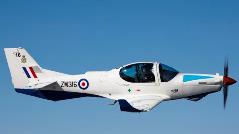 A white RAF Prefect aircraft flying in the blue sky.