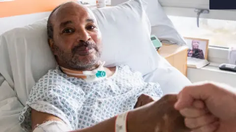 RCSLT The picture shows a person resting while fist pumping another individual recovering from surgery to his throat. 