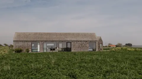 Anne Jones Cabin in situ in the middle of a green clifftop field.