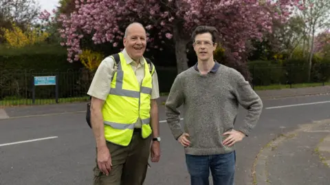 Facundo Arrizabalaga The two residents stand on the side of the road, with blossom trees seen in the background