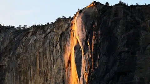 A waterfall glowing orange as the as the setting sun illuminates the mist of the falls, making them appear to be on fire