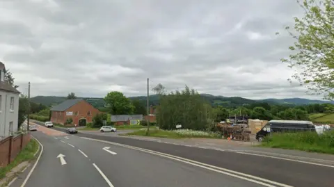 A road junction with directional arrows indicating the right hand lane is for turning right and the left hand lane is for travelling straight on. There are buildings either side, 