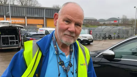 Matthew Gudgin/BBC Richard Bussien, a man who is looking at the camera. He is wearing a blue top and darker blue fleece and a fluorescent hi-vis jacket. 