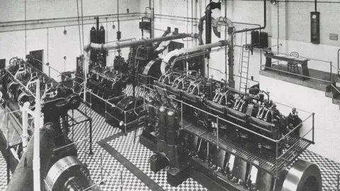 Supplied Black and white image of a large generator machinery inside a generator hall.