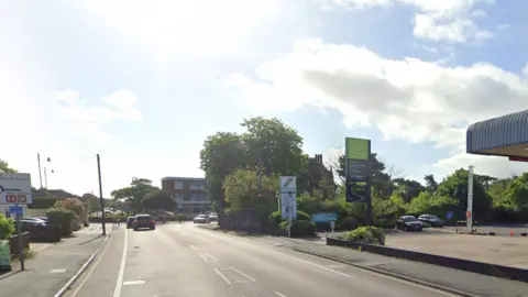 A general view of High Road West in Felixstowe. It shows a road leading up to a roundabout with a petrol station to the right. Cars can be seen travelling along the road.