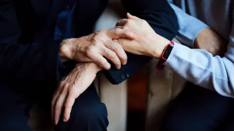 A stock image of a person holding hands with an elderly person. 