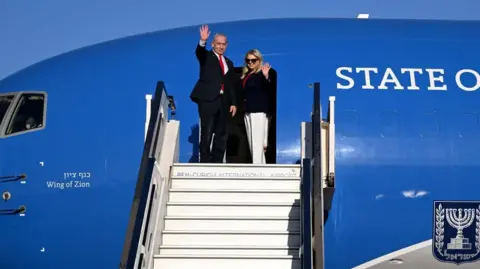 Avi Ohayon/GPO Israeli Prime Minister Benjamin Netanyahu and his wife Sara wave before boarding an Israeli government flight to Washington, at Tel Aviv Ben Gurion airport in Israel (6 June 2025)