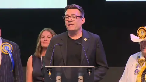 Andy Burnham standing on stage in Wigan
