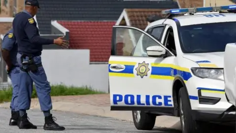 South Africa Police Service Police officers dressed in official uniform standing near their car with an open door  