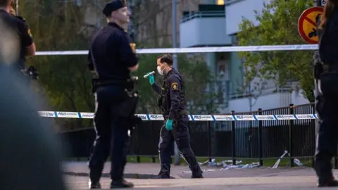 Getty Images Police, including one with a torch, stand outside between two strips of police tape