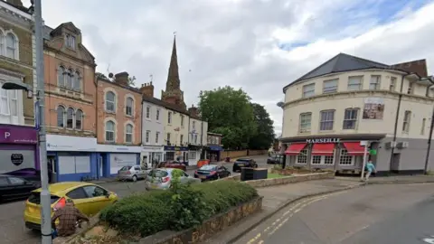 Google Three-storey terraced buildings with businesses on the ground floor. A bush is in the foreground.