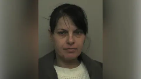 Tracey Makings with medium-length dark hair, a white jumper and a grey jacket, looking at the camera in a police custody photo.