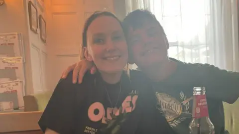 Tammy Tammy, a woman wearing a black T-shirt, with Noah sitting next to her smilng for the camera, while his arm around Tammy.