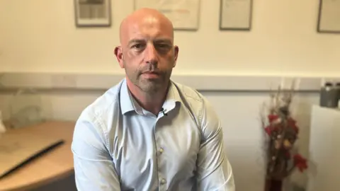 Edd Terrey wearing a light grey shirt sat in an office at the Gilmorton supported living service in Leicester 