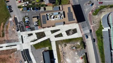 Chris Haig A birds-eye drone photo of boulevard, which is grey and has cars, buildings and vacant land on each side