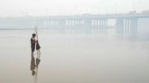 Reuters A small boy sets a fishing trap, with a bridge over the Ravi River in the background, amid smog in Lahore.