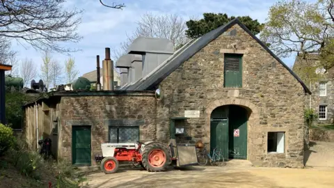 A building with green doors and a red tractor outside on the island of Sark.