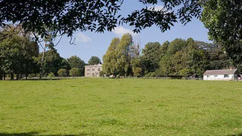 Peter Facey / Geograph A large meadow with Wintershill Hall in the distance - a large mansion house surrounded by mature trees