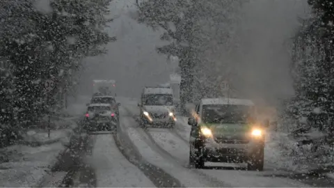 Getty Images Cars driving on a road through a wooded area during a blizzard 