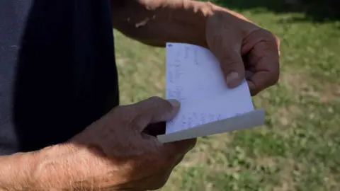 Francesco Tosto/BBC Dmytro's father holds a note they received from their son while he was held by Russia, reading "I'm alive, I'm well. Everything's ok" 