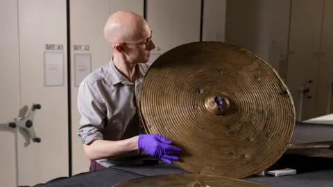 Dr Matthew Knight holding up a circular bronze shield found in a field in Beith more than 200 years ago.