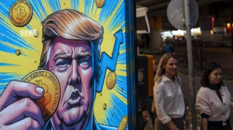 Getty Images Cartoon image of US President-elect Donald Trump holding a Bitcoin token displayed at a Coinhero store in Hong Kong.