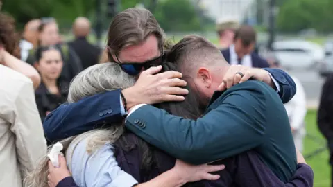 Reuters Virginia Giuffre's brothers, Sky Roberts and Danny Wilson, and her sisters-in-law, Lanette Wilson and Amanda Roberts, hug during a "butterfly" vigil commemorating the one-year anniversary of the death of Virginia Roberts Giuffre. 
