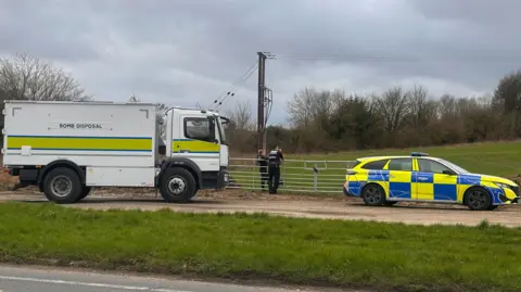 A picture of a bomb disposal lorry and police van outside a field, where the bomb was detonated. 