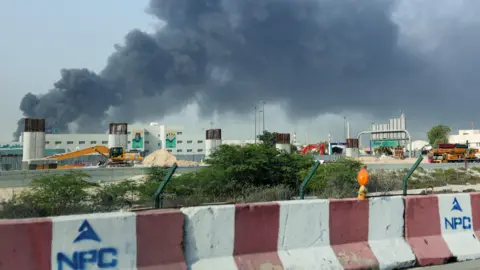 People run across a road with black smoke in the background. 