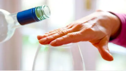 A woman hold her hand over an empty wine glass as someone offers to pour her a glass of wine. 