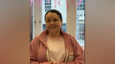 Woman with a pink striped top and pink jacket in front of a shop window.