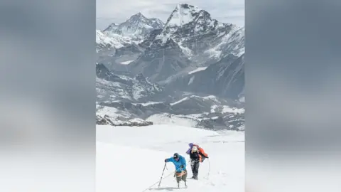 Abiral Rai Two men - one with prosthetic legs - scale a snowy mountainous landscape.
