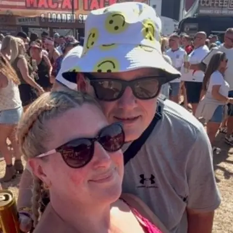 Supplied Michael Osbourne and Yvette Osbourne in front of festival goers. He is wearing a hat and grey t-shirt. They both have glasses on.