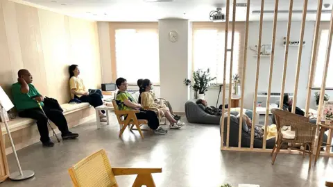 Jake Kwon/ BBC People sitting on chairs and beanbags and watching a movie together.