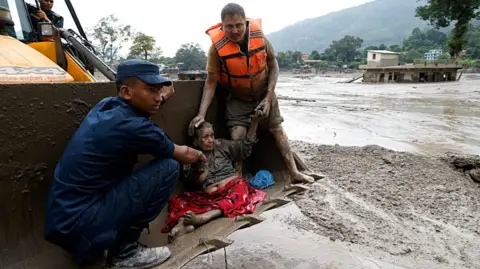 Rescuers transport an elderly woman on heavy machinery amidst flash floods