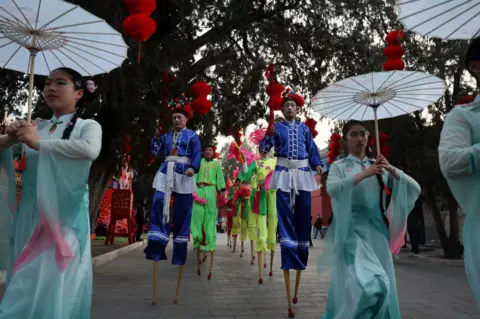 Florence Lu/Reuters Women carry umbrellas and men walk on the pillars of people at a ceremony in Beijing, China